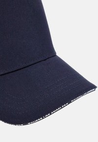Gorra azul marino hecha de un tejido texturizado con visera curva. Presenta una marca blanca a lo largo del borde y detalles de costura visibles.