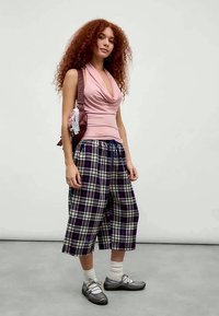 Top roz, drapat, asociat cu pantaloni culotte cu carouri, în nuanțe de bleumarin și alb. Pantofi gri cu curele și șosete albe completează ținuta.