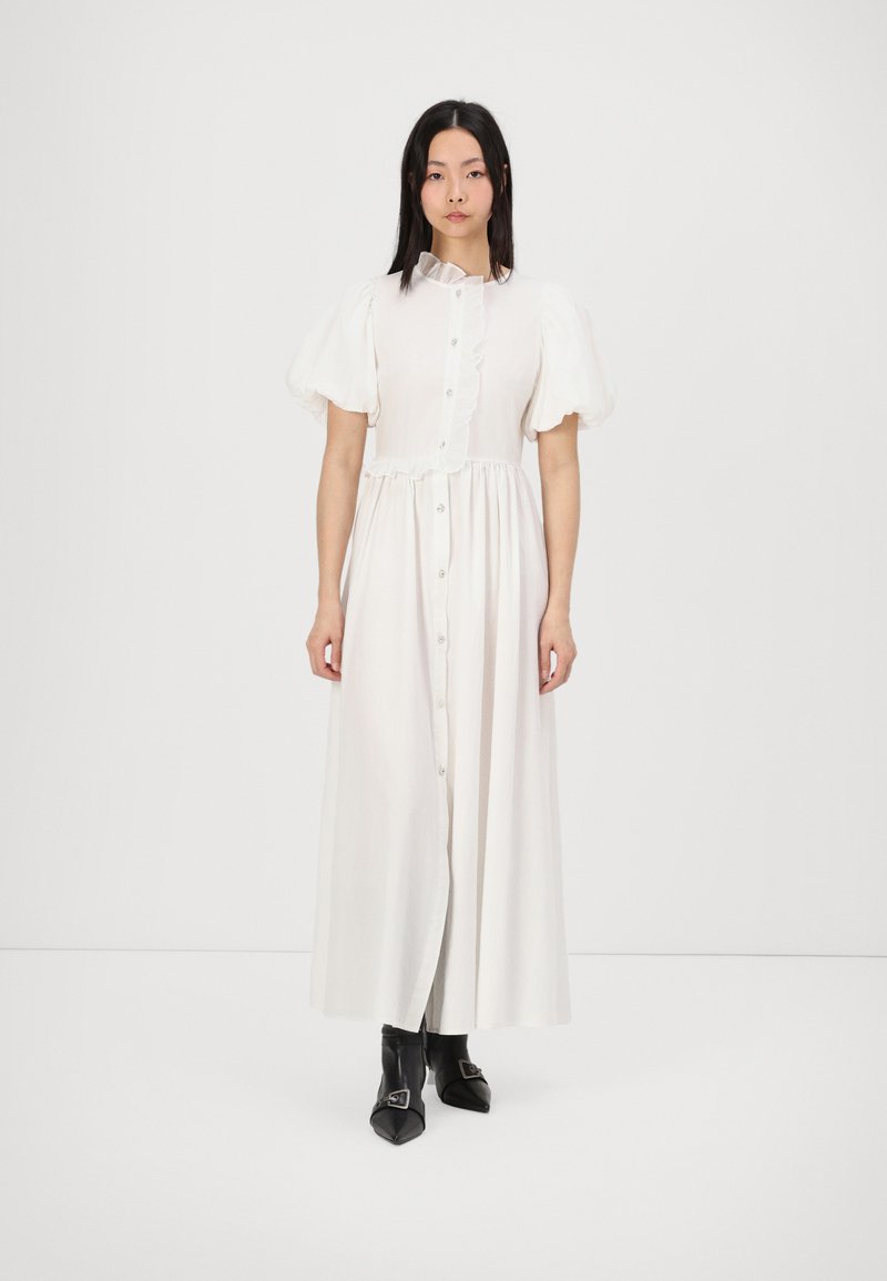 Vit klänning med puffärmar och volangkrage, knappslå framtill och svängig silhuett, kombinerad med svarta spetsiga ankelbooties.