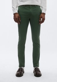 Πράσινο βαμβακερό παντελόνι με στενή εφαρμογή. Διαθέτει επίπεδη μπροστινή όψη, θηλιές για ζώνη και κλείσιμο με μονό κουμπί. Συνδυάζεται με σκούρα καφέ παπούτσια.