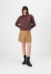 Brun genser med rund hals, kombinert med gul-brun rutete shorts; svarte snøring ankelsko; minimalt med maskinvare detaljer.