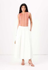 Pink striped neule top ilman hihoja, yhdistettynä pitkään valkoiseen hameeseen. Malli käyttää vaaleanpunaisia korkokenkiä ja pitää käsissään ruskeaa laukkua.