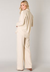 Beige blouse met lange mouwen en een kraag, gecombineerd met een wijde broek. Licht, textuurstof met een comfortabele pasvorm en een achternaaddetail.