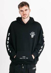 Schwarzer Kapuzenpulli mit Fronttasche, weißes Grafikdesign auf der Brust und dem Ärmel, oversized Schnitt, Mischgewebe aus Baumwolle. Textdetails am Saum.
