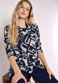 Top de color azul marino con un patrón gris abstracto y texturizado. El diseño presenta un cuello de barco y mangas largas, elaborado con una tela suave.