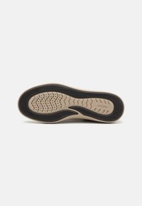 Semelle de chaussure avec une base beige et des bords en caoutchouc noir. Présente un motif texturé avec des rainures et de petits trous de ventilation.