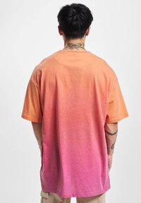 Kortermet T-skjorte med en gradient fra oransje til rosa, laget av bomull. Har en løs passform og glatt stofftekstur.