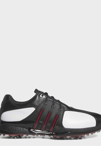 Black and white golf shoe with black laces and red accents on the sides, featuring cleats on the sole for traction.
