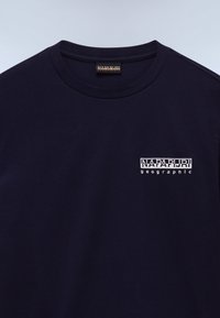 Camiseta de algodón azul marino con cuello redondo y mangas cortas. Presenta un logo bordado blanco en el área del pecho izquierdo. Textura suave.