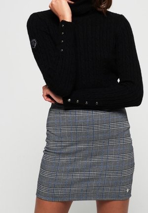 Un pull noir à col montant côtelé avec des détails de boutons sur les manches ; associé à une mini-jupe grise à carreaux avec des accents bleus et une coupe cintrée.