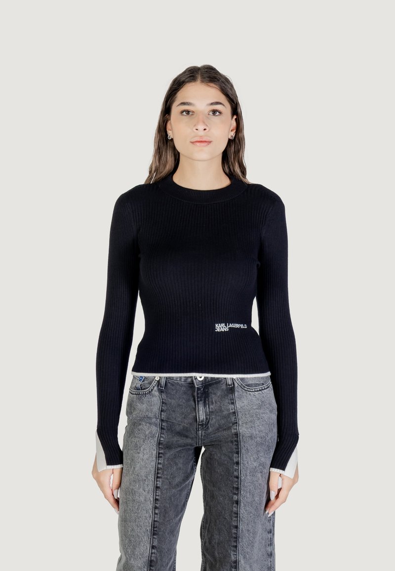 Pull noir à manches longues côtelé avec un col ras du cou et un détail logo blanc à la taille, associé à un jean gris au design bicolore.