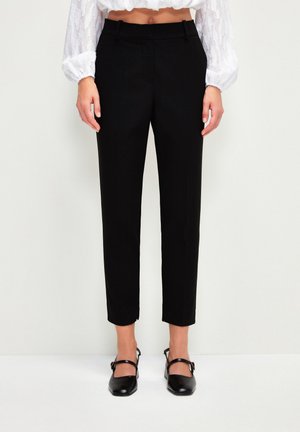 Person wearing high-waist black ankle-length trousers, white cropped long-sleeve blouse, and black low-heeled Mary Jane shoes.