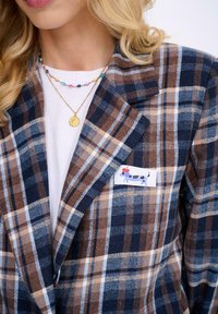 Hnědý a námořnický kostkovaný sako s klopovým límcem, na kapsičce s potiskem kresleného psa. Doplněné barevnými korálkovými náhrdelníky.