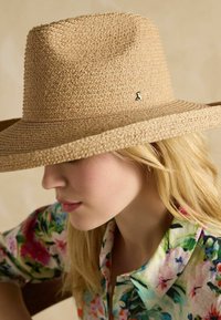 Pălărie cu boruri largi din paie în culoare naturală, cu o țesătură texturată și un mic accent metalic pe lateral. Design moale, casual.