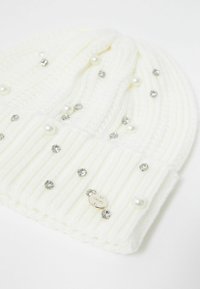 Beanie bianco lavorato a maglia con texture a coste, decorato con perle e strass. Etichetta metallica del marchio attaccata sul davanti.