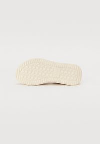 Suola di una scarpa, texturizzata con un motivo a rombi, caratterizzata da una forma curva e di colore crema chiaro, con il marchio impresso sul lato.