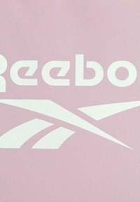 Logo y texto blanco de Reebok sobre fondo de tela rosa claro texturizada.
