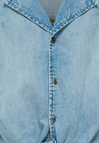 Ljusblå denimskjorta med klassisk krage, fem knappar fram, och en knuten detalj vid midjan. Mjuk textur och slitstarkt tyg.