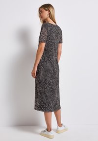 Leopard print midi dress with short sleeves, made of lightweight fabric. Features a relaxed fit and falls below the knee. Paired with white sneakers.