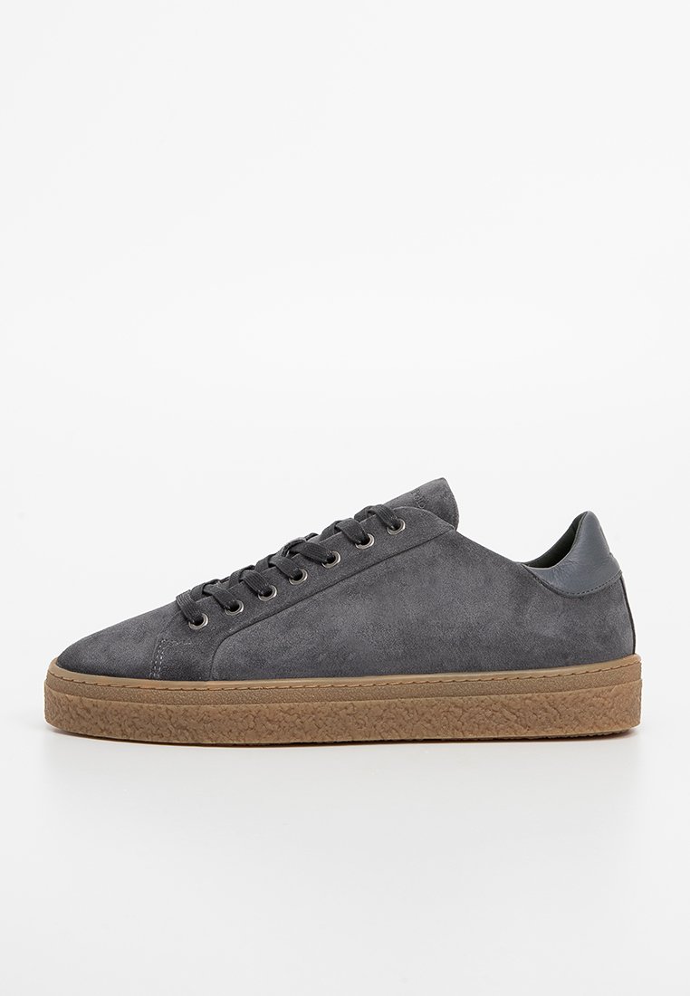 Szare zamszowe sneakersy niskie z teksturowaną brązową gumową podeszwą, okrągłym noskiem i płaskimi sznurowadłami. Charakteryzują się minimalistycznym designem i smukłym profilem.