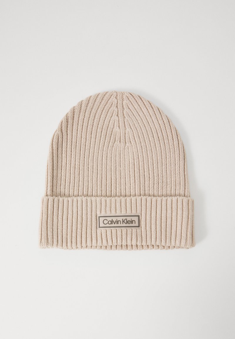 Knit beige beanie with a ribbed texture and a folded brim. A label with "Calvin Klein" is stitched on a rectangular patch.