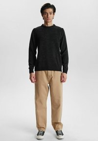 Schwarzer gestrickter Pullover mit einem gerippten Rundhalsausschnitt, kombiniert mit beigen, lockeren Hosen und schwarzen Sneakers. Einfaches Design, ohne Muster.