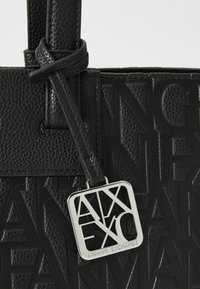 Black textured leather tote bag featuring embossed logo design and a silver tag with "Armani Exchange." Straps are black with a knotted detail.