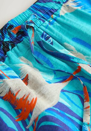 Blå og teal shorts med snor i taljen, prydet med et trykt design af fugle og abstrakte bølger i kontrasterende farver.