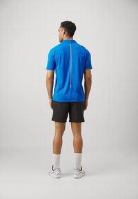 Kortærmet polo shirt i lys blå med krave og en vertikal farveaccent i midten af ryggen. Sammen med sorte shorts.