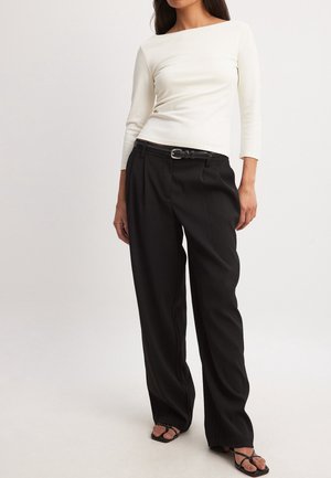 Lange mouwen, ivoorkleurig topje met een boothals gecombineerd met zwart, hooggetailleerde, geplooide broek en zwarte sandaaltjes met bandjes. Getextureerde stof.