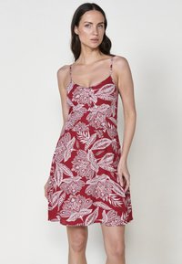 Rotes ärmelloses Kleid mit weißen Blumenmustern, einem taillierten Oberteil und einem schwingenden Rock. Der Stoff wirkt leicht und hat verstellbare Träger.