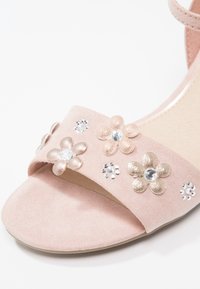 Sandale rose à bout ouvert avec une bride décorée d'appliques florales métalliques et scintillantes ornées de strass clairs au centre.