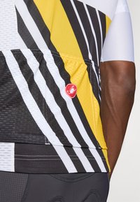 Sykkeltrøye med et teksturert mesh-design i svart, hvitt og gult diagonalt mønster. Inkluderer en rød logoaccents.