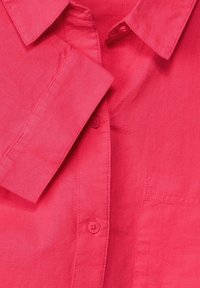 Chemise en lin fuchsia avec un col standard, devant boutonné et poche poitrine. Caractérisée par une texture lisse et des détails de couture visibles.