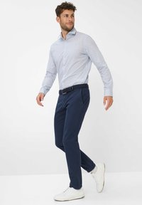 Lichtblauw shirt met kleine geometrische patronen, marineblauwe broek en witte sneakers. De outfit heeft een geweven zwarte riem en een relaxte pasvorm.