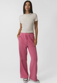 T-shirt à manches courtes côtelé beige clair et pantalon de jogging rose avec poches latérales, taille à cordon, et détails de couture visibles.