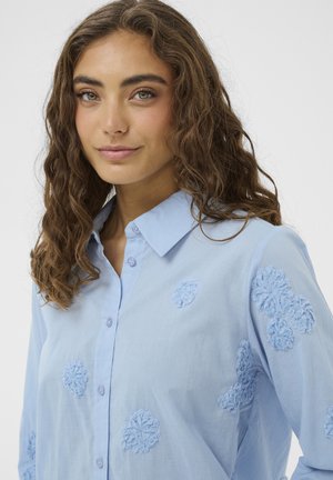 hele sinise kraega särk nööpide sulgemisega, millel on tikitud lillemustrid sobivas toonis ja pehme tekstuuriga kangas.