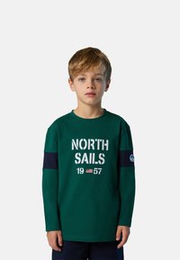Grünes langärmliges T-Shirt mit "NORTH SAILS 1957" in Weiß bedruckt. Mit navyblauen Akzenten an den Ärmeln und einem runden Logo am Arm.