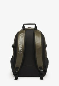 Sac à dos noir et olive avec une texture lisse, doté d'une poignée supérieure, de bretelles réglables et d'un logo imprimé sur le panneau avant.