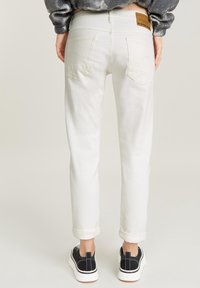 Vita denimjeans med medelhög midja, raka ben, uppvikt fåll och bakfickor. Har en läderlogga på midjebandet.