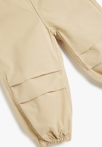 Beige cargo bukser med elastiske manchetter, udstyret med store sidelommer og et glat bomuldsstof, designet til komfort og bevægelsesfrihed.