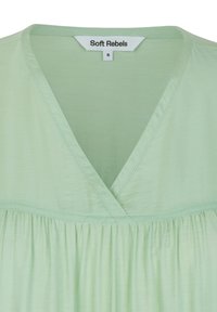 Blouse vert clair avec un col en V, des détails plissés à l'ourlet et une texture douce. L'étiquette indique "Soft Rebels", taille petite.