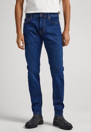 Mørkeblå denimjeans med slim fit, med frontlommer og kontrasterende oransjefargede sømmer, sammen med sorte ankelsko.