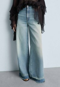 Wide-leg denim jeans in light blue with a faded finish, featuring raw hem edges and a high waist design.