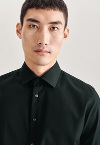 Donkergroene button-up shirt met een gestructureerde kraag en lange mouwen, gemaakt van een gladde stof met een subtiele glans. Zilveren knopen accentueren de voorkant.