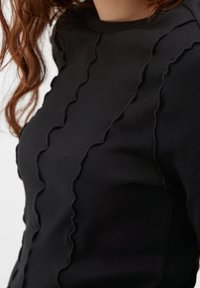 Musta ribbattu pitkähihainen paita, jossa on aaltoilevat tekstuuritikkaukset edessä, tiukka muotoilu ja pyöreä pääntie.