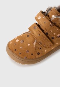Zapato marrón para niño pequeño con lunares metálicos, doble correa de Velcro, suela de goma y interior suave, sobre un fondo blanco.