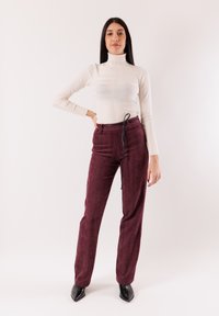 Dolcevita beige aderente con righe testurizzate; pantaloni vinaccia a vita alta con coulisse nera e gambe dritte; scarpe nere con punta appuntita.