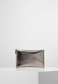 Metallinen hopeinen suorakulmainen clutch-laukku, jossa on sileä pinta ja rakenteellinen muotoilu. Vetoketjukiinnitys ylhäällä. Yksinkertainen ja moderni estetiikka.