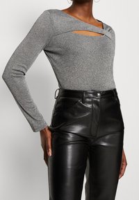 Top grigio a maniche lunghe con motivo a coste e taglio; abbinato a pantaloni in pelle nera a vita alta con tasche laterali e texture liscia.